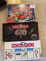 Three Monopoly board games stacked: Here & Now Limited Edition on top, Star Wars Limited Collector's Edition in the middle, Original Monopoly at bottom with classic design.