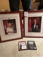 Two framed portraits, one of Queen Elizabeth II and one of Prince Philip, along with two DVDs on a carpeted floor.
