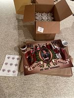 Open box with packing material, yard sign and mugs placed on floor showing design