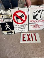 Four framed metal signs shown individually or in groups with secure holes for mounting. Signs displayed on carpeted floor with visible hands holding them for scale.