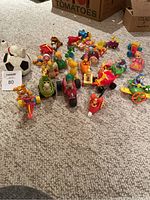 Group photo of all small toys laid out on carpet including Snoopy and other characters.