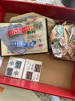 Collection of stamps spread out including a green album, a box of loose stamps, and sheets with stamps.
