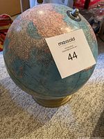 Photo showing globe on carpeted floor with partial view of surrounding area, Top view of the globe with the seller's lot card on it
