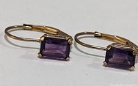 Close-up photo of pair of 10K gold earrings with rectangular amethyst stones.