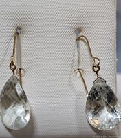 Front view of the pair of earrings showing pear-shaped faceted light green amethyst stones set in 14K gold hooks.