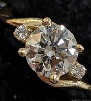 Front-facing close-up of center round brilliant diamond with side stones in prong setting on gold band