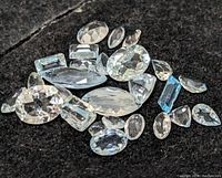 Photo of multiple aquamarine gemstones scattered on black surface, showing various cuts and shapes.