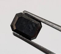 Emerald cut black diamond held in tweezers showing table and step facets