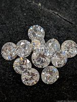 Close-up image of multiple loose round cubic zirconia stones placed on a dark fabric background showing their faceted brilliance.