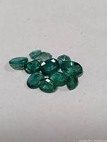 Close-up of 11 small genuine emerald gemstones showing various cuts and clarity.