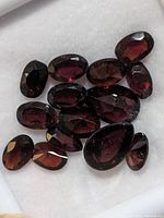 Close-up photo showing 12 faceted garnet stones arranged on white fabric, showing color and cut detail.