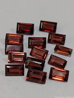 Close-up of multiple rectangular cut garnet loose gemstones on a white surface showcasing their deep red transparent color and faceted surfaces.