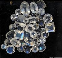 Top-down image showing assorted faceted moonstone gemstones with various shapes and showing blue flash on black background.