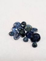 Array of multiple faceted sapphire gemstones showing variation in size, shape and color.