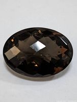 Close-up image of the oval faceted smokey quartz gemstone showing the checkered faceting pattern and deep smoky brown color.