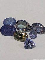 Seven genuine tanzanite gemstones of varying shapes and cuts displayed on a flat surface in good light.
