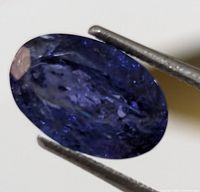 Close-up of the oval tanzanite gemstone showing its color and inclusions while held in tweezers.