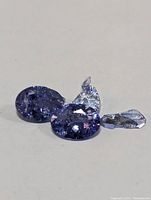Three oval-cut Tanzanite stones placed on a white surface, showing chips and damage on the stones.