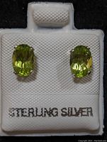Photo showing pair of oval light green peridot stone stud earrings set in sterling silver with "STERLING SILVER" text on holder.