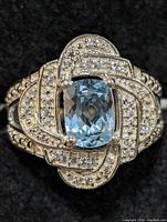 Close-up front view of sterling silver ring featuring a blue topaz center stone surrounded by clear pavé stones in an intricate looped design.