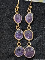 Front view of both earrings showing the three linked faceted oval amethyst gemstones each set in silver bezels.
