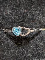 Close-up front view of sterling silver ring with heart-shaped blue topaz and open heart design on a black background.
