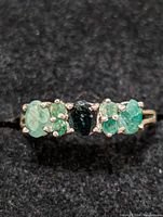 Close-up front view of sterling silver ring with multiple green stones on black fabric.