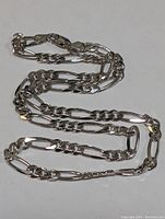 Full view of the sterling silver men's necklace with Figaro chain links laid flat against white background.