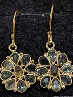 Close up photo of one side of the flower-shaped sterling silver earring with multicolor pear-shaped tourmaline stones set in a gold-tone finish, displayed against a dark fabric background.