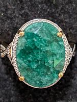 Close-up front view of the ring showing large oval green emerald surrounded by diamonds with gold prongs.