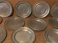 Eleven pewter plates arranged side by side showing raised rimmed edges and aged patina