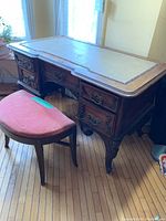 Full view of antique desk with leather top and demi-lune bench with pink upholstery in front