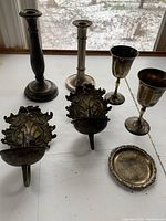 Photo showing all items together on a table near window: two tall candle holders, two goblets, two ornate wall candle holders, small dish.