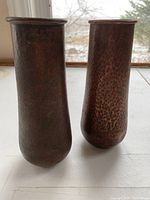 Pair of hand hammered copper vases shown standing side by side on a white surface with natural light from window.