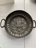 Top-down photo of the antique pewter shallow dish showing two handles and detailed crest with anchor.