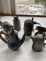 Photo of five antique pewter vessels including teapot, tankards, and pitcher showing overall lot condition and variety.
