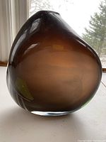 Front and side views of the smoky brown glass vase displaying organic asymmetrical shape and subtle green details, under natural light by window.