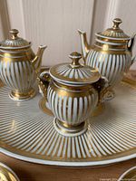 Close-up photo showing teapot, creamer, and sugar bowl on tray, details of gold gilt decoration and lid knobs