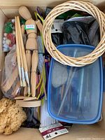 Photo showing a drawer with wooden mannequins, paint brushes, wicker rings, pipe cleaners, a sponge, and a plastic container with craft tools.