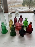 Overview of eleven miniature glass bottles on white surface near window with outdoor background