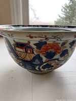 Side view of the ceramic bowl showing blue and coral patterns with traditional architectural motifs and a rimmed edge.