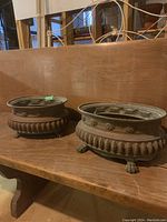 Pair of oval metal planters with detailed ornamentation, placed on a wooden surface.