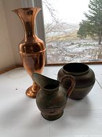 Wide view of all three copper vases showing differences in shape and condition with visible dents on tall vase and patina on smaller vases.