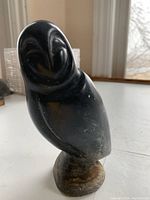 Front and side views of a black soapstone owl sculpture with natural color variations on a lighter stone base.
