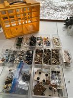 Full collection of various buttons organized in clear compartments inside a yellow carrying case, showing a wide assortment of colors and materials.