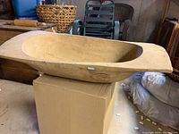 Large handcarved wooden dough bowl placed on cardboard box, showing oval interior and natural wood finish.