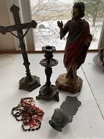 Overview of statue, crucifix, candlestick, rosaries, and holy water font on shelf
