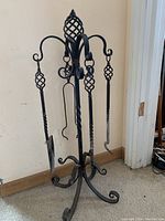 Full view of wrought iron fireplace tool set with four tools hanging on stand featuring twisted and braided elements.