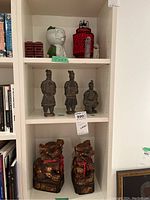 Full shelf view showing three terracotta warrior figures and a pair of carved wooden foo dogs at the bottom.