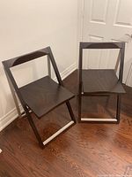 Pair of matching foldable chairs with dark wood and metal frame, showing in an upright position on a hardwood floor.
